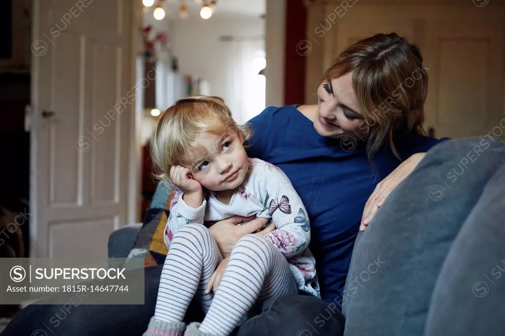 Mother and little daughter sitting together on the couch at home