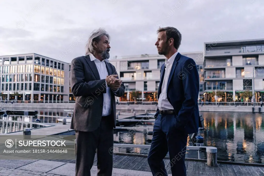 Two businessmen talking at city harbor at dusk