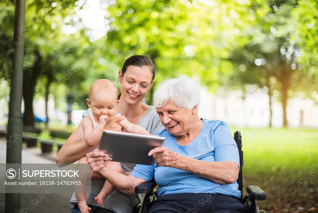 Grandmother, daughter and granddaughter having fun with tablet in a park