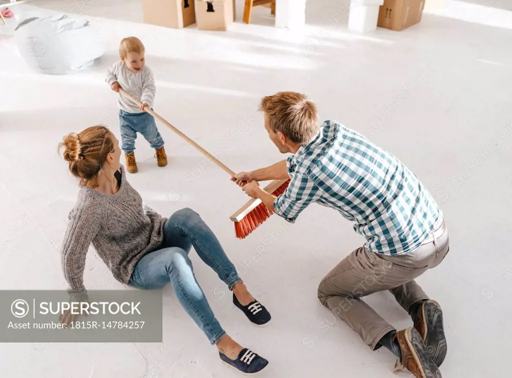 Father and daughter having fun with a broom in a loft