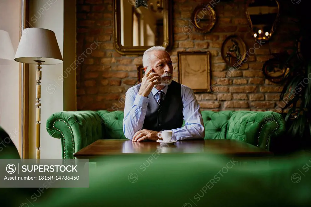 Elegant senior man sitting on couch in a cafe on cell phone