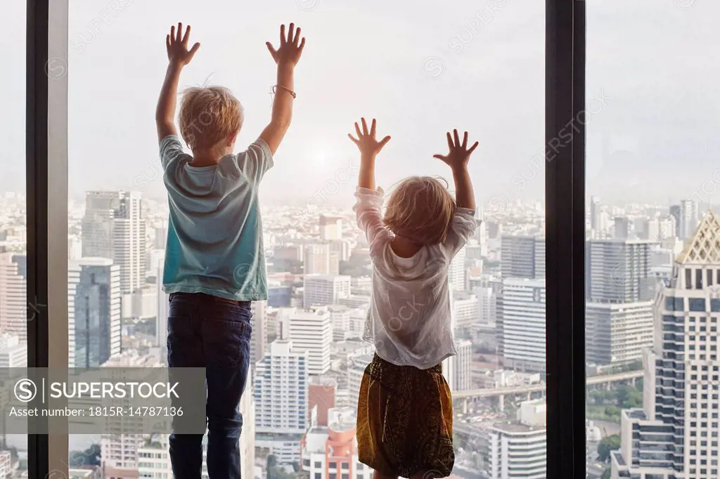 Thailand, Bangkok, boy and little girl looking through window at cityscape