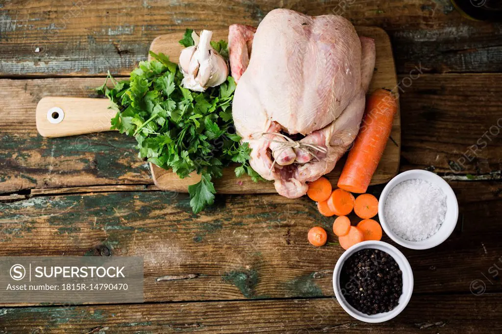 Raw chicken with carrots, parsley, garlic, pepper and salt on a chopping board