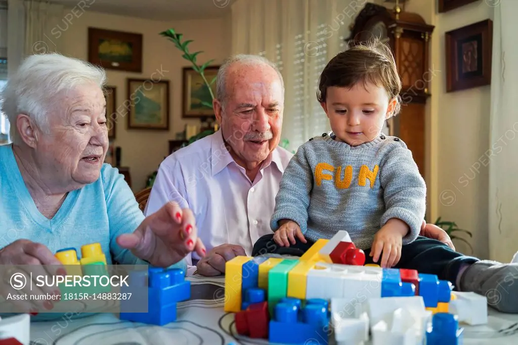 Great-grandparents and baby girl playing together with plastic building bricks at home