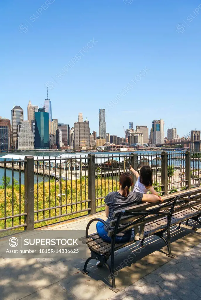 USA, New York, Brooklyn, Back view of woman and young girl sitting on bench while looking the skyline of Manhattan from Brooklyn