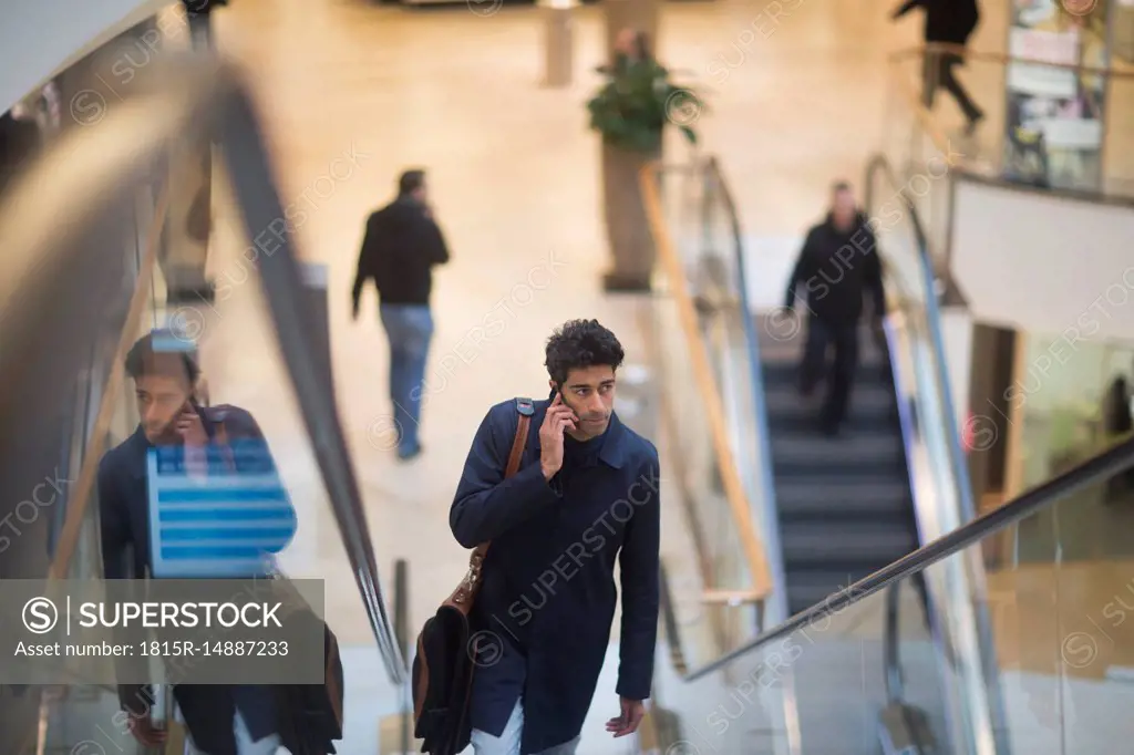 Man on the phone standing on escalator in a shopping mall