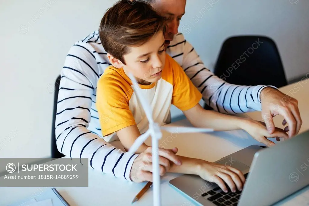 Father and son using laptop next to wind turbine model