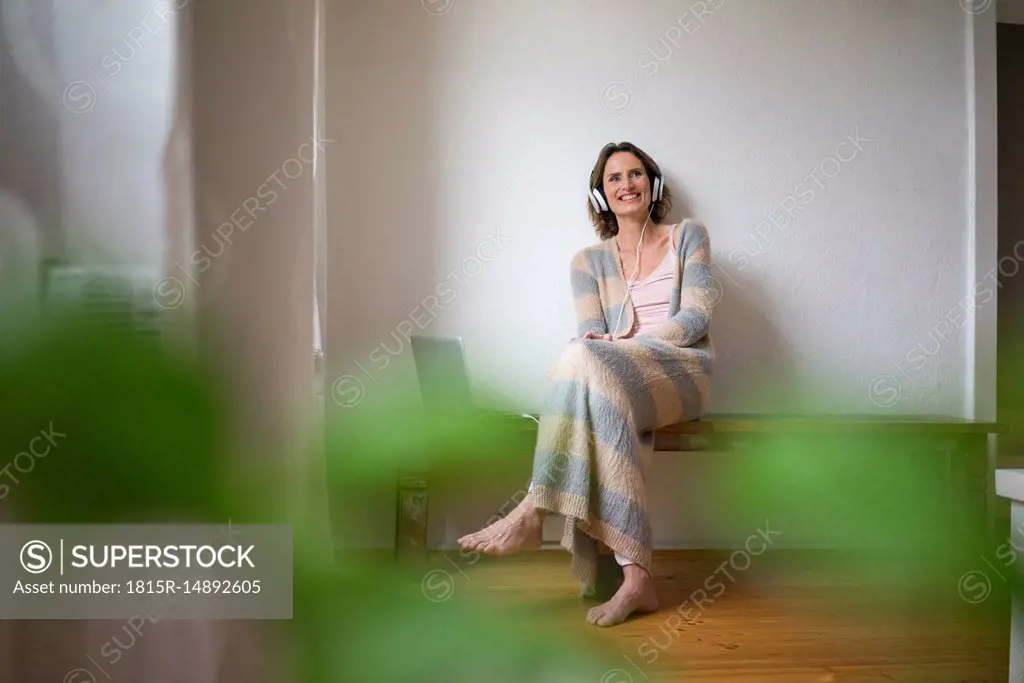 Smiling mature woman sitting on wooden bench at home listening to music