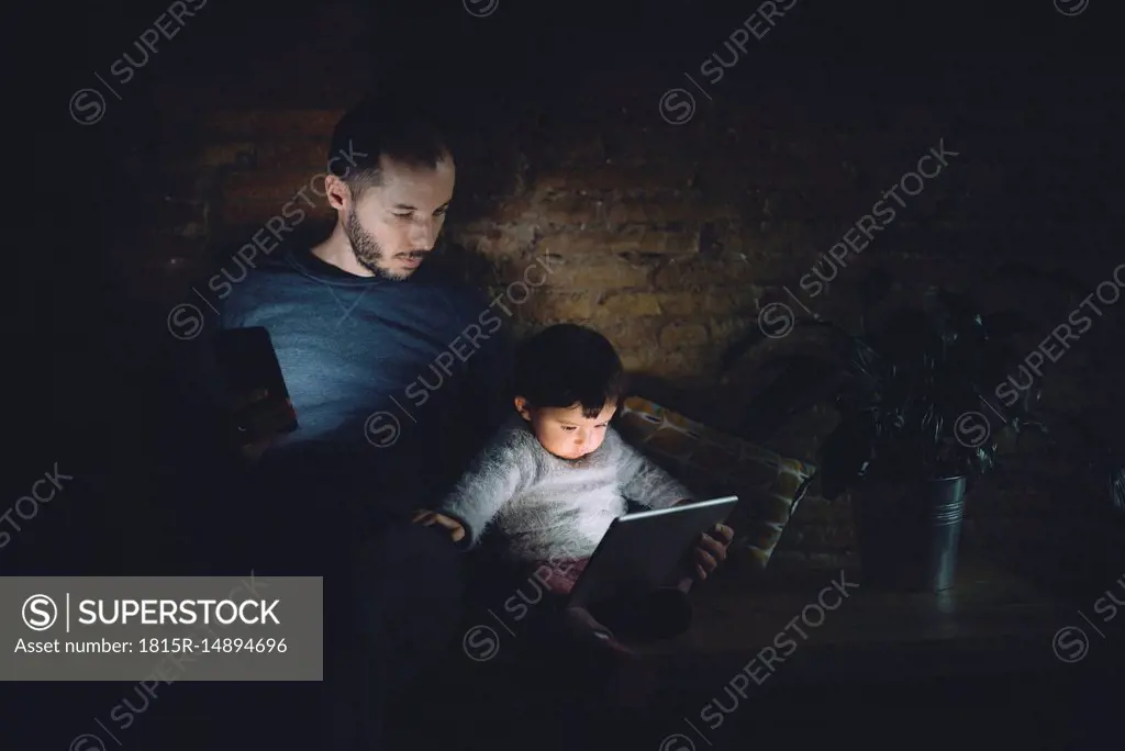 Father and daughter looking at digital tablet at home in the dark