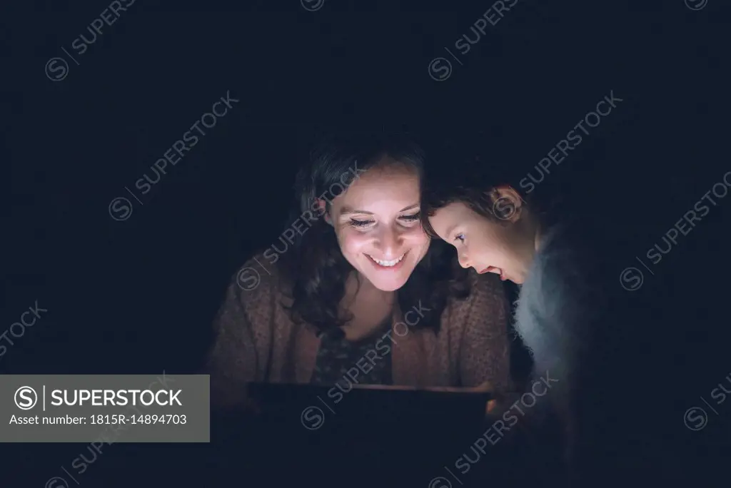 Mother and daughter using digital tablet at home in the dark