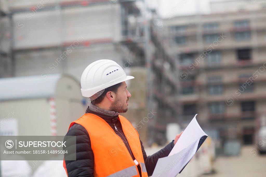 Man with plan wearing safety vest and hard hat at construction site -  SuperStock