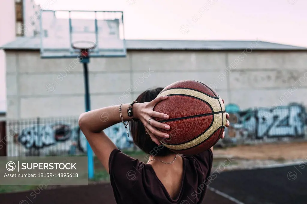 Rear view of young woman holding basketball on outdoor court