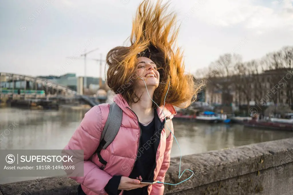 Paris, France, happy young woman listening music with earphones and smartphone tossing her hair