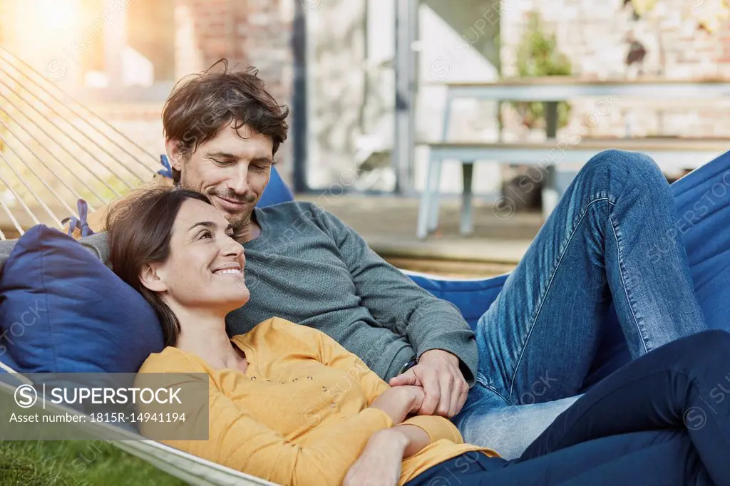 Smiling couple lying in hammock in garden of their home