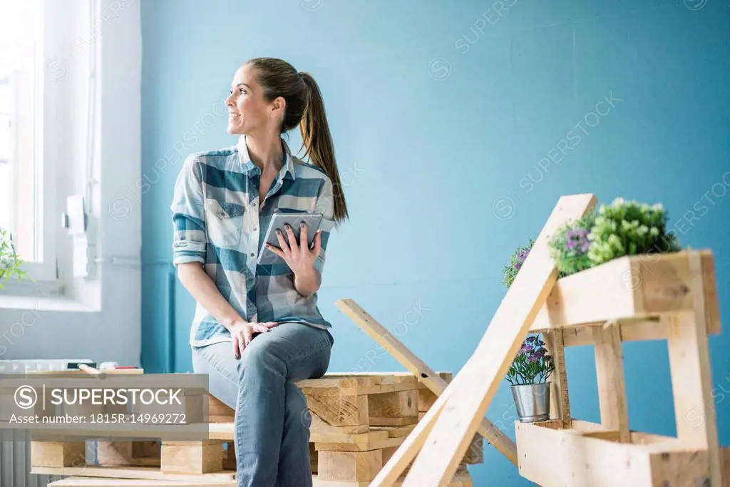 Woman refurbishing her new home with pallets, holding digital tablet