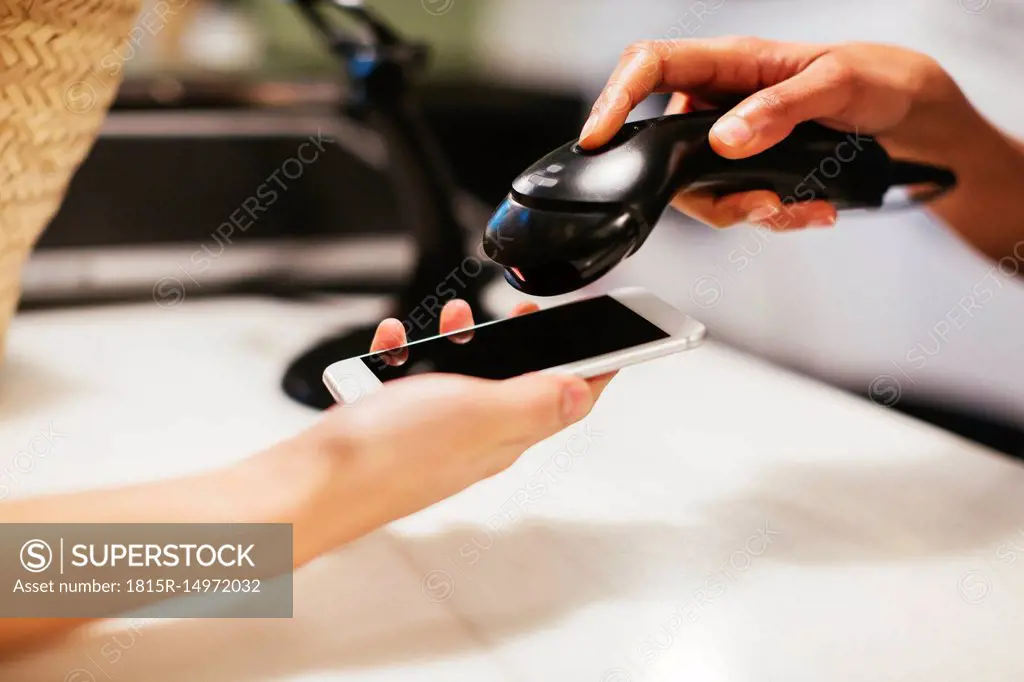 Close-up of customer paying cashless with smartphone at counter of a store