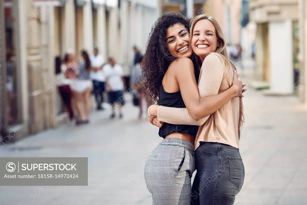 Portrait of two happy friends hugging each other on the street