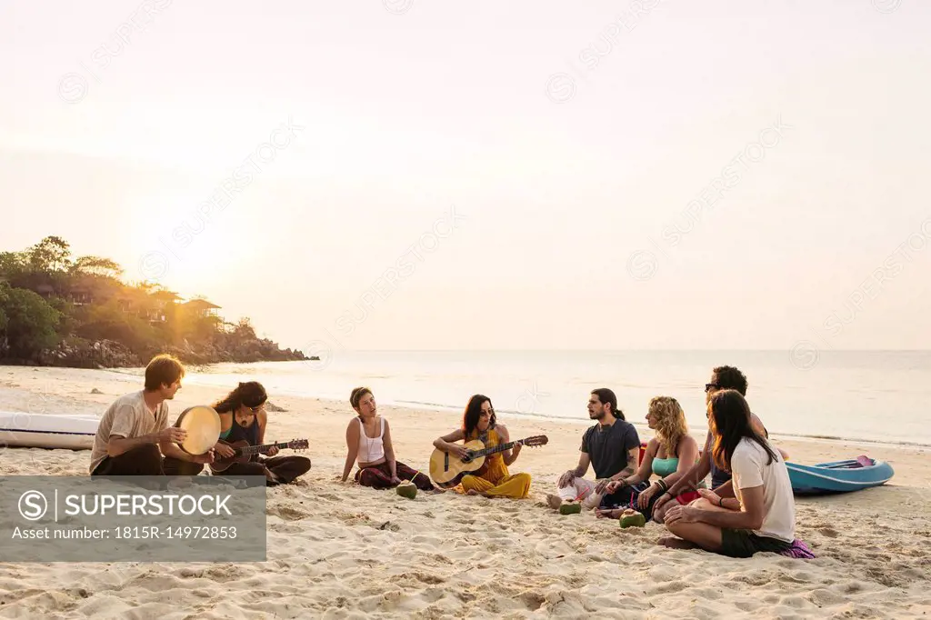 Thailand, Koh Phangan, group of people sitting on a beach with guitar at sunset