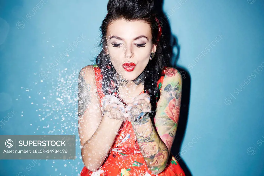 Portrait of tattooed woman blowing artificial snow