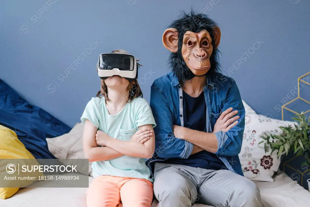 Father wearing monkey mask sitting next to son wearing VR glasses at home