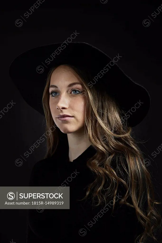 Portrait of young woman wearing black hat and clothes against black background