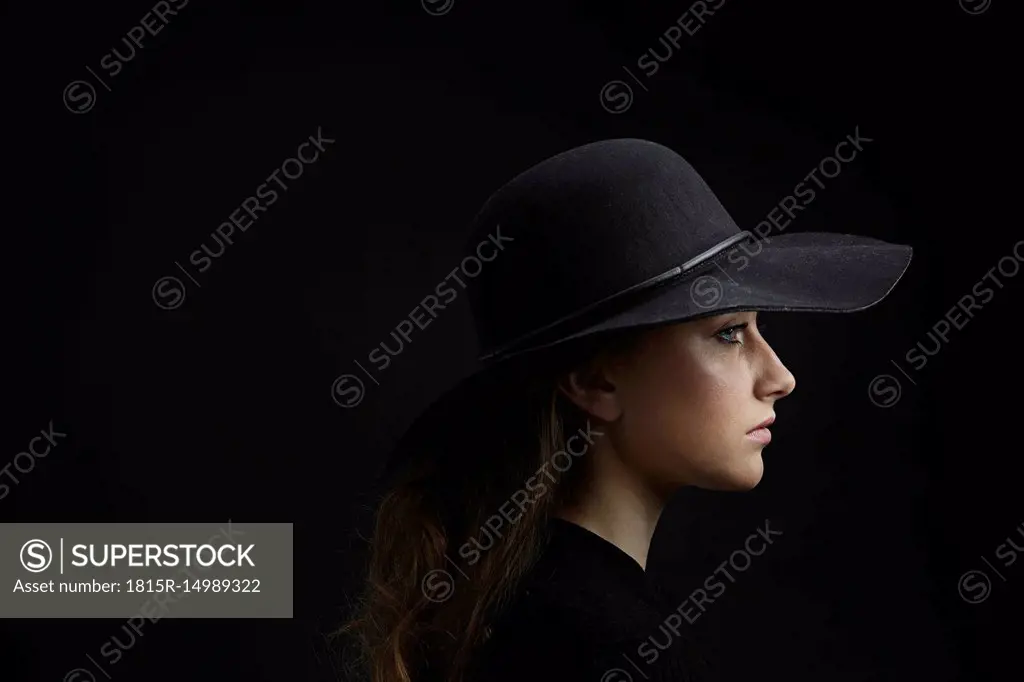 Profile of sad young woman wearing black hat against black background