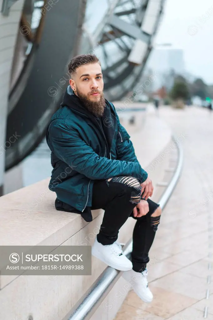 France, Paris, portrait of bearded young man sitting on a wall