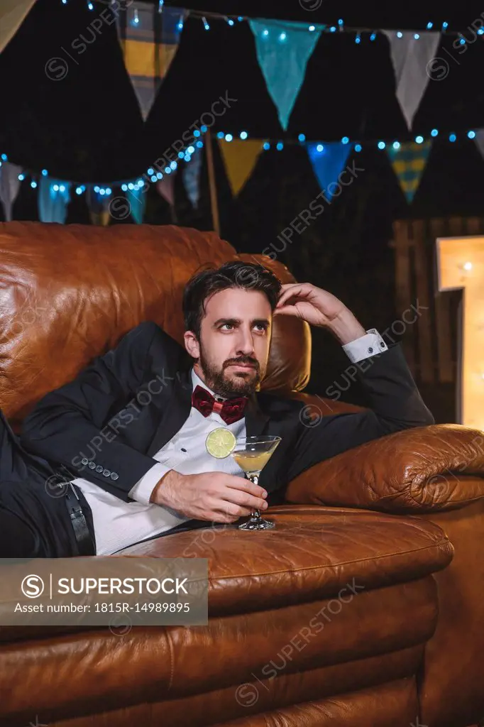 Pensive man in suit lying on sofa on a night party oitdoors