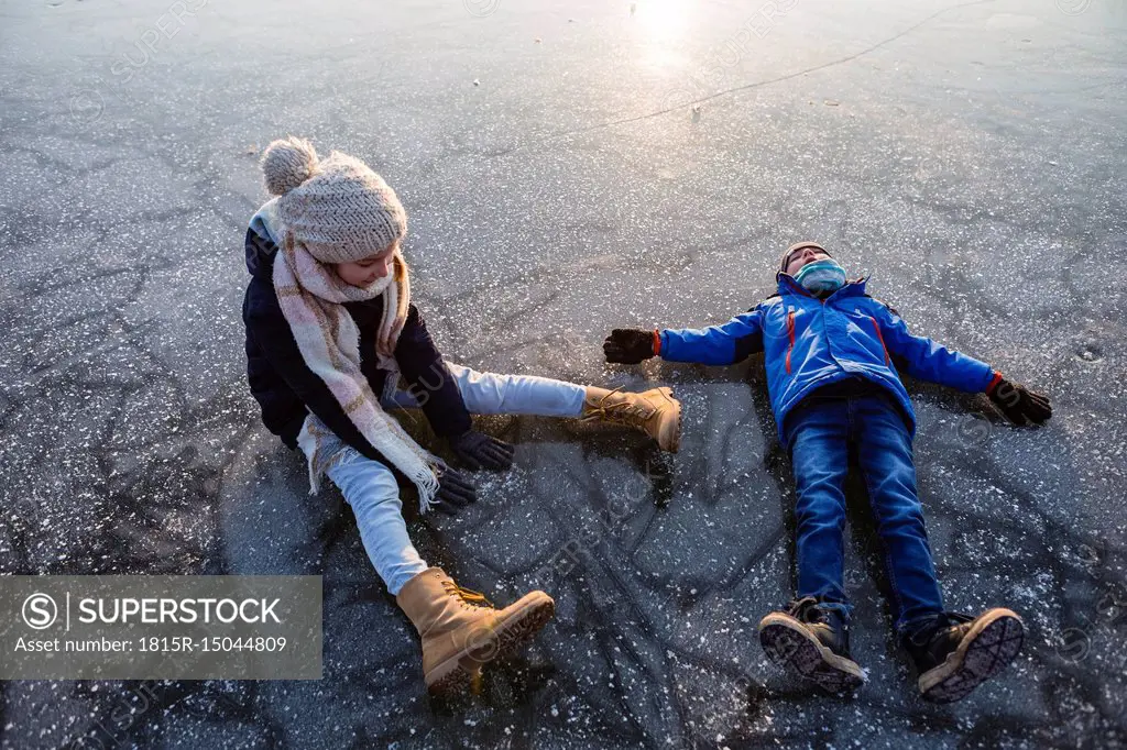 Germany, Brandenburg, Lake Straussee, two kids sitting and lying down on frozen lake