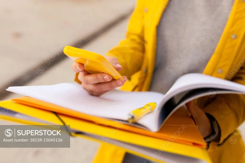 Close-up of woman with cell phone and folder outdoors