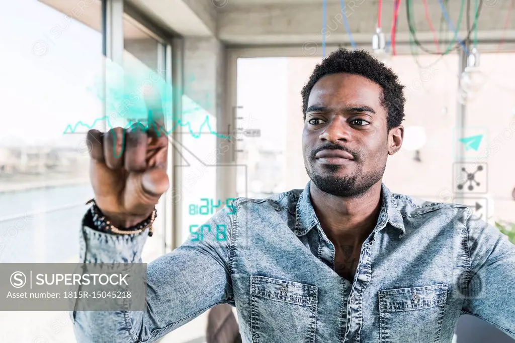 Casual businessman touching glass pane with data in office