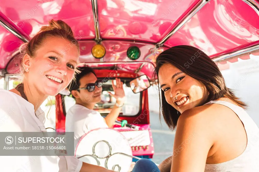 Thailand, Bangkok, portrait of smiling friends riding tuk tuk