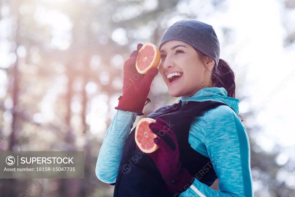 Portrait of laughing young woman wearing sportswear holding two halves of grapefruit