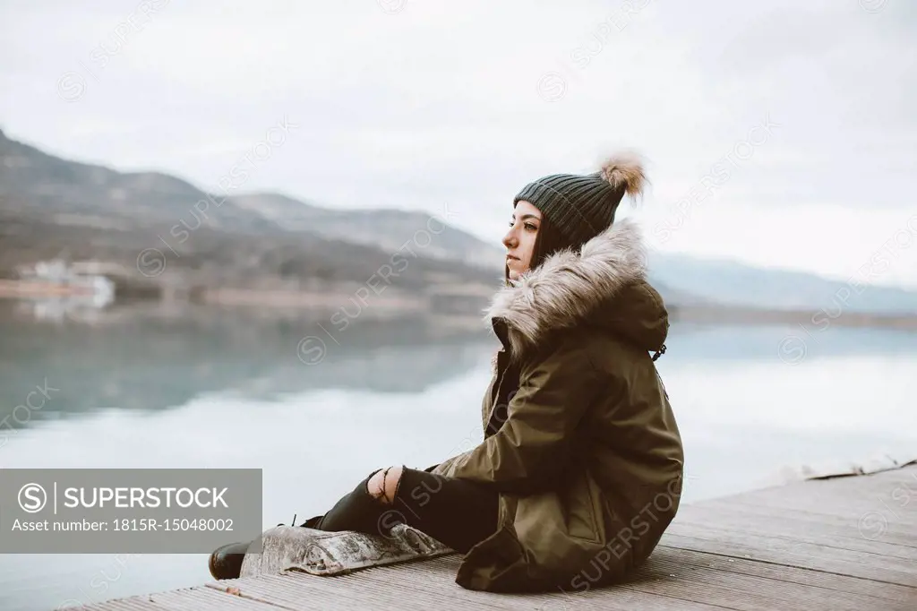 Pensive young woman sitting on jetty looking at distance