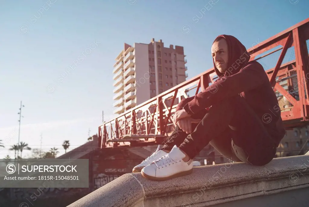 Man with hoodie sweater sitting on wall