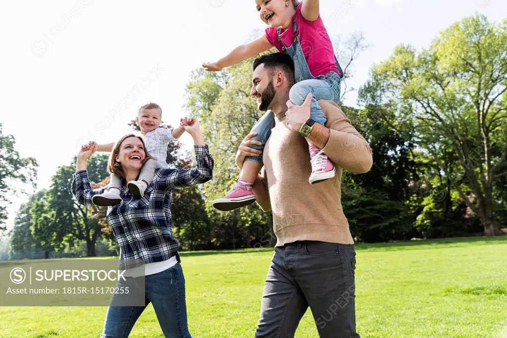 Happy parents carrying children on shoulders in a park