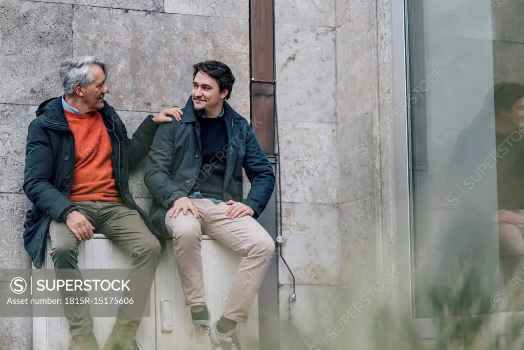 Confident senior man and young man sitting in the city talking