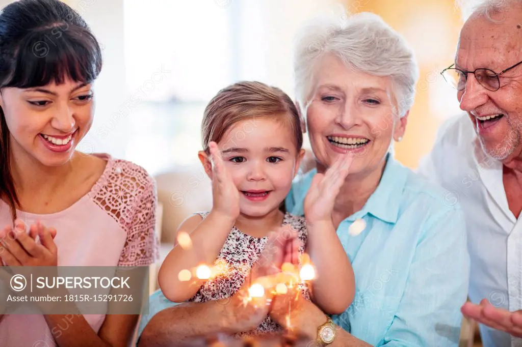 Little girl lwatching sparklers on a birthday cake, sitting on grandmother's lap