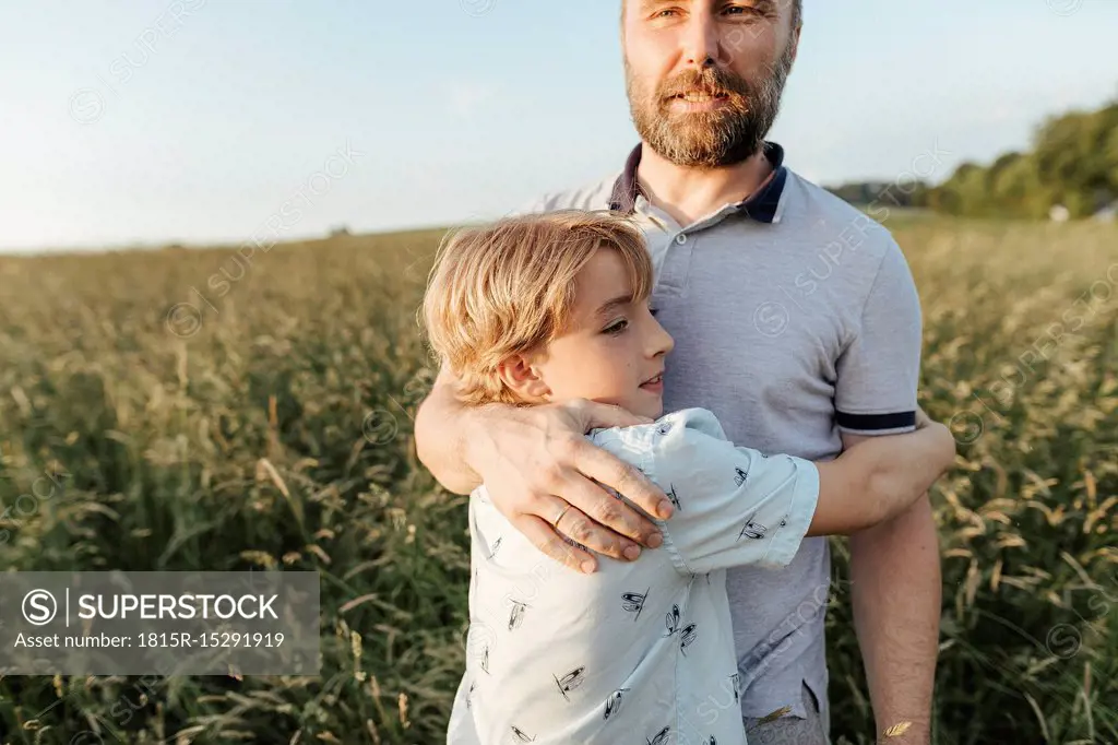 Father and son standing on a meadow hugging each other