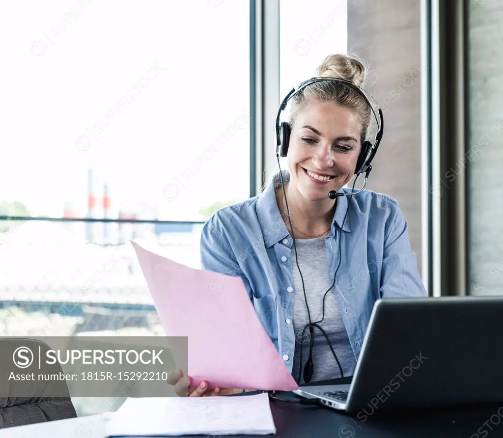 Young businesswoman sitting at desk, making a call, using headset and laptop