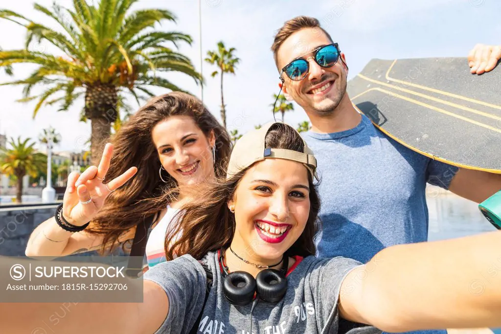 Selfie of three happy friends with skateboard