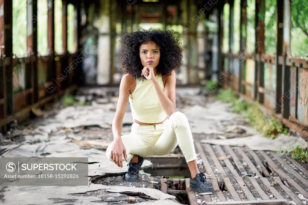 Portrait of fashionable young woman crouching in abandoned and destroyed old train