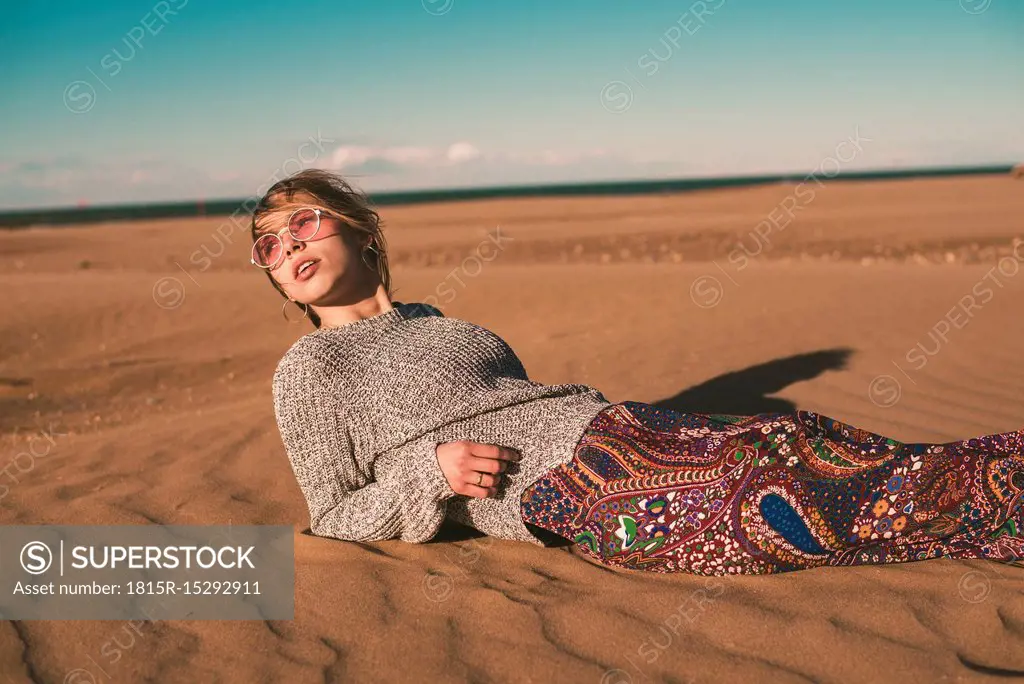 Spain, fashionable young woman wearing sunglasses lying on the beach