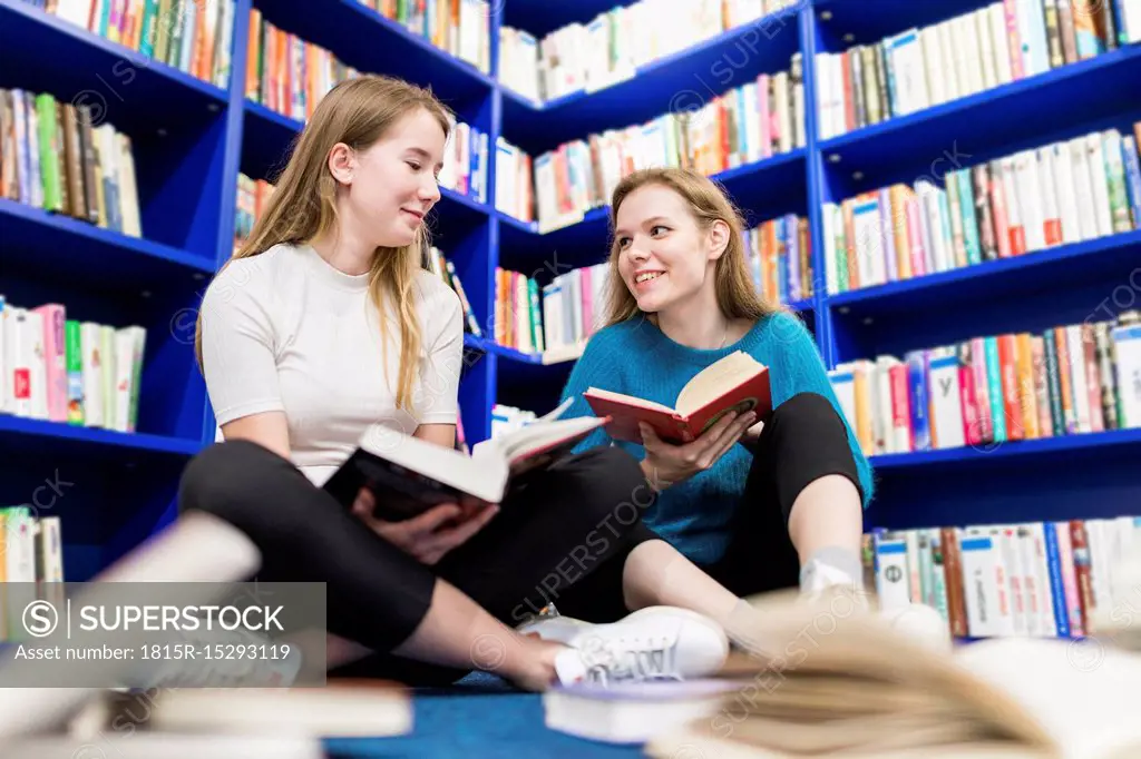 Two teenage girls with books sitting on the floor in a public library