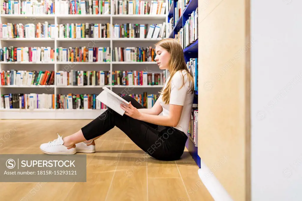 Teenage girl sitting on the floor in a public library reading book