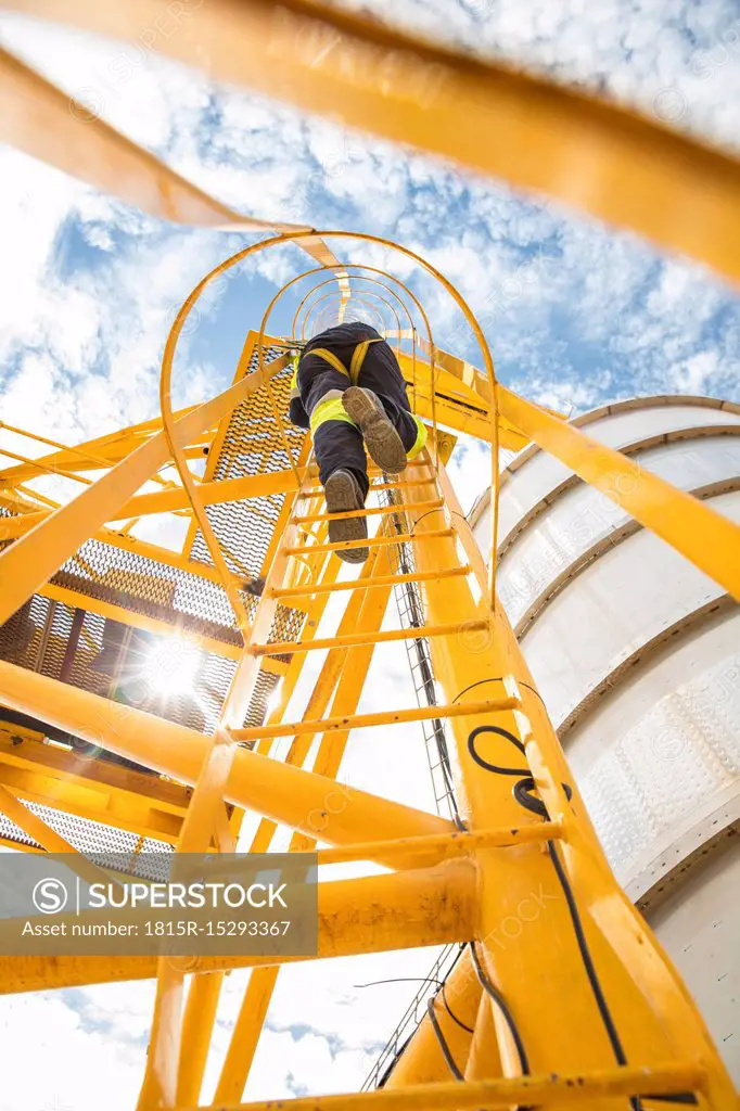 Worker climbing up ladder at tank