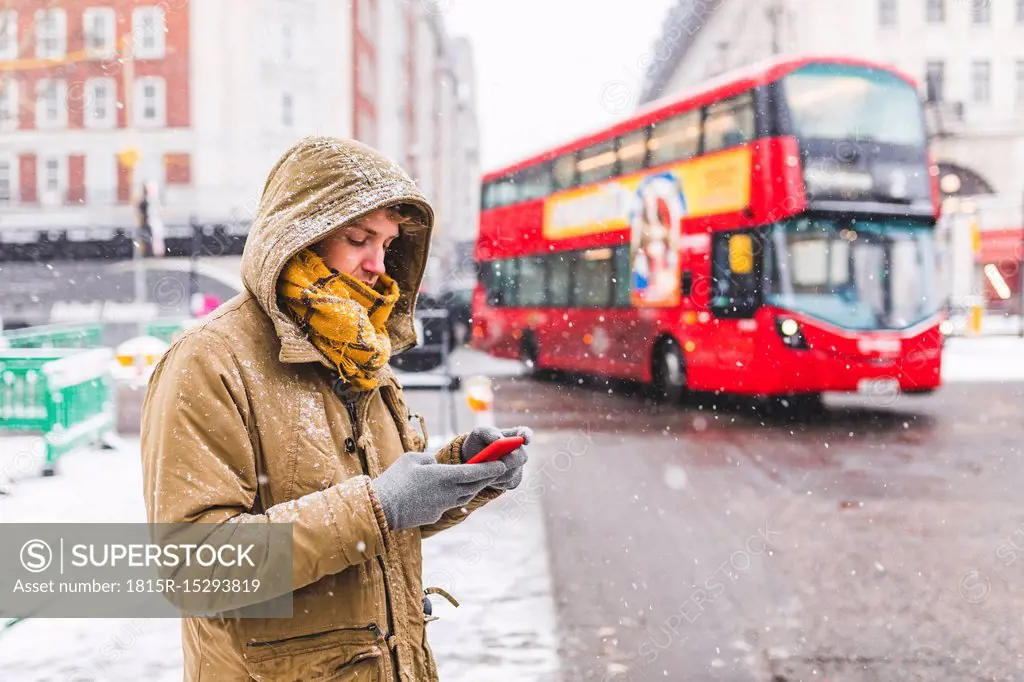 UK, London, young man standing next to the road in the city looking at cell phone