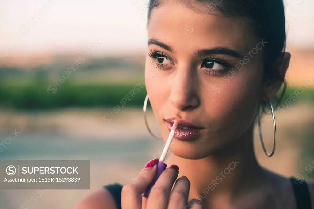 Portrait of teenage girl in nature applying lip gloss