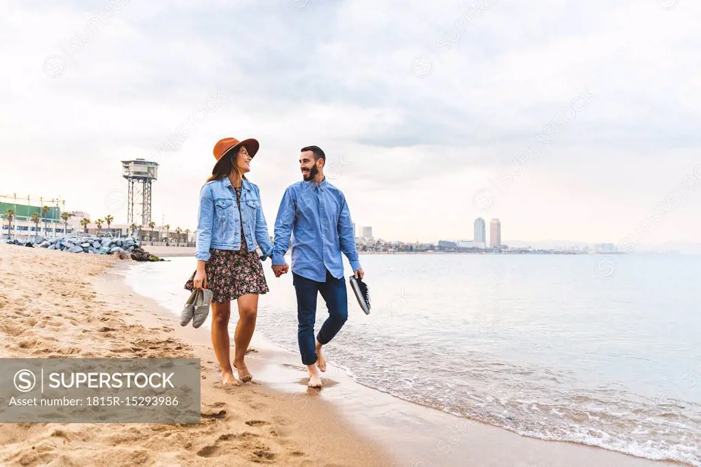 Spain, Barcelona, couple walking barefoot on the beach