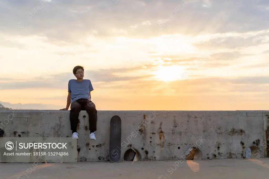 Young Chinese man sitting on wall at sunrise